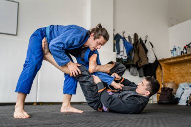 İki Brezilyalı jiu jitsu BJJ sporcusu akademi dövüş sanatları sahasında antrenman yapıyor kimono gi spor üniforması giyiyorlar spor minderlerinde spor jiujitsu ve kendini savunma konsepti fotokopi uzayı