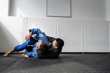 İki Brezilyalı jiu jitsu BJJ sporcusu akademi dövüş sanatları sahasında antrenman yapıyor kimono gi spor üniforması giyiyorlar spor minderlerinde spor jiujitsu ve kendini savunma konsepti fotokopi uzayı