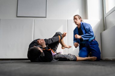 İki Brezilyalı jiu jitsu BJJ sporcusu akademi dövüş sanatları sahasında antrenman yapıyor kimono gi spor üniforması giyiyorlar spor minderlerinde spor jiujitsu ve kendini savunma konsepti fotokopi uzayı