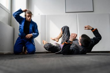 İki Brezilyalı jiu jitsu BJJ sporcusu akademi dövüş sanatları sahasında antrenman yapıyor kimono gi spor üniforması giyiyorlar spor minderlerinde spor jiujitsu ve kendini savunma konsepti fotokopi uzayı