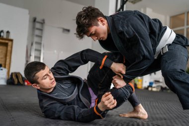 İki Brezilyalı jiu jitsu BJJ sporcusu akademi dövüş sanatları sahasında antrenman yapıyor kimono gi spor üniforması giyiyorlar spor minderlerinde spor jiujitsu ve kendini savunma konsepti fotokopi uzayı