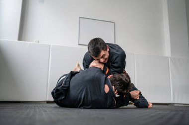 İki Brezilyalı jiu jitsu BJJ sporcusu akademi dövüş sanatları sahasında antrenman yapıyor kimono gi spor üniforması giyiyorlar spor minderlerinde spor jiujitsu ve kendini savunma konsepti fotokopi uzayı