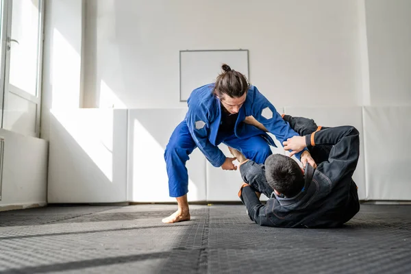 İki Brezilyalı jiu jitsu BJJ sporcusu akademi dövüş sanatları sahasında antrenman yapıyor kimono gi spor üniforması giyiyorlar spor minderlerinde spor jiujitsu ve kendini savunma konsepti fotokopi uzayı