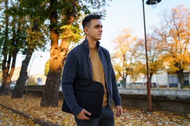 Sonbahar günü elinde iş çantasıyla duran beyaz bir adamın yan görüntüsü. Gerçek insanlar. Genç iş adamı işe ilk gün gidiyor.