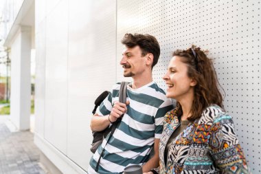 Gündüz öğrencileri ya da turistler beyaz duvarın önünde poz veren erkek ve kadın genç çift bıyıklı beyaz erkek ve kız arkadaş mutlu bir gülümsemeyle birbirleriyle konuşuyorlar.