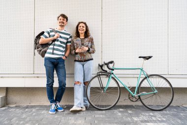 Gündüz öğrencileri ya da turistler beyaz duvarın önünde poz veren erkek ve kadın genç çift bıyıklı beyaz erkek ve kız arkadaşı kameraya bakıp gülümsüyor.