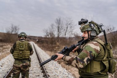 Savaş köpeklerinden iki asker paralı asker üniformalı silahlı adamlar savaş alanında çatışma bölgesinde demiryolunu emniyete alırken görev sırasında devriye bölgesini gözlüyor.