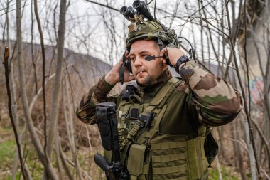 Kamuflaj üniformalı bir askerin cephedeki portresi. Silahlı ve savaş alanına gitmeye hazır. Doğada duruyor, paralı askerlerin kamera köpeklerine bakıyor ya da gönüllü.