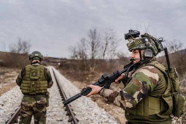 Savaş köpeklerinden iki asker paralı asker üniformalı silahlı adamlar savaş alanında çatışma bölgesinde demiryolunu emniyete alırken görev sırasında devriye bölgesini gözlüyor.