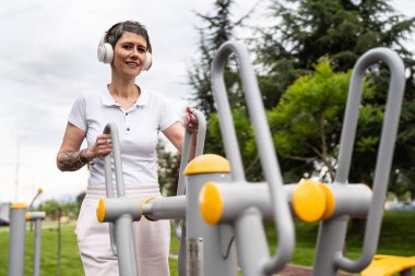 Gündüz bina önünde kısa saç eğitimi alan modern, olgun bir kadın spor salonunda eliptik eğitim makinesi simülatöründe sağlıklı yaşam tarzı konsepti sunuyor.