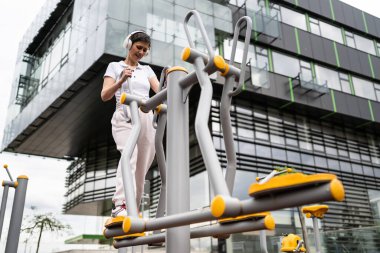 Gündüz bina önünde kısa saç eğitimi alan modern, olgun bir kadın spor salonunda eliptik eğitim makinesi simülatöründe sağlıklı yaşam tarzı konsepti sunuyor.