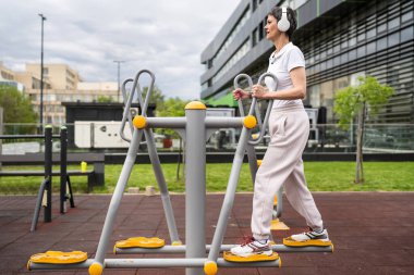 Gündüz bina önünde kısa saç eğitimi alan modern, olgun bir kadın spor salonunda eliptik eğitim makinesi simülatöründe sağlıklı yaşam tarzı konsepti sunuyor.