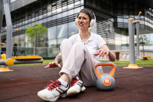 Modern olgun, kısa saçlı, beyaz bir kadın açık hava spor salonunda kettlebell ağırlığıyla oturmuş spor antrenmanı yaptıktan sonra fren yapıyor sağlıklı yaşam tarzı konsepti fotokopi çekiyor.