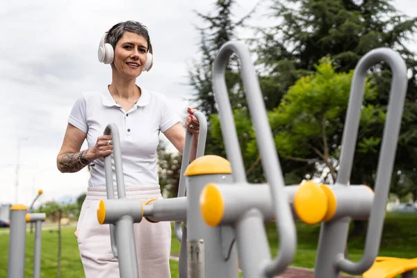 Gündüz bina önünde kısa saç eğitimi alan modern, olgun bir kadın spor salonunda eliptik eğitim makinesi simülatöründe sağlıklı yaşam tarzı konsepti sunuyor.