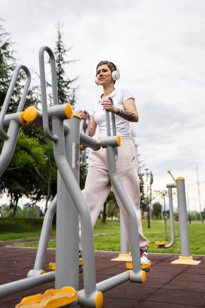 Gündüz bina önünde kısa saç eğitimi alan modern, olgun bir kadın spor salonunda eliptik eğitim makinesi simülatöründe sağlıklı yaşam tarzı konsepti sunuyor.