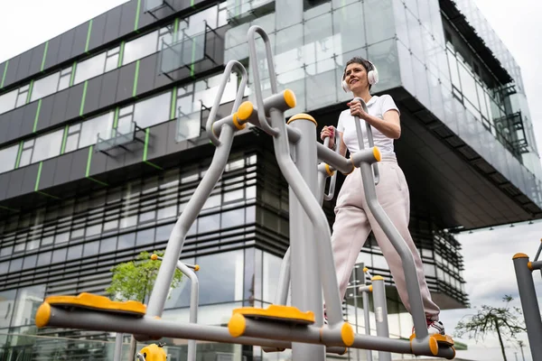 Gündüz bina önünde kısa saç eğitimi alan modern, olgun bir kadın spor salonunda eliptik eğitim makinesi simülatöründe sağlıklı yaşam tarzı konsepti sunuyor.