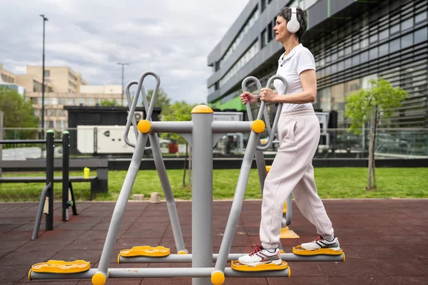 Gündüz bina önünde kısa saç eğitimi alan modern, olgun bir kadın spor salonunda eliptik eğitim makinesi simülatöründe sağlıklı yaşam tarzı konsepti sunuyor.