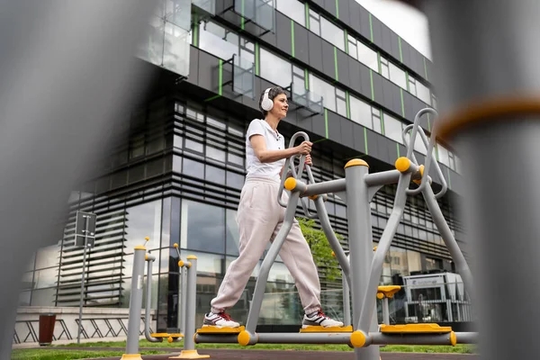 Gündüz bina önünde kısa saç eğitimi alan modern, olgun bir kadın spor salonunda eliptik eğitim makinesi simülatöründe sağlıklı yaşam tarzı konsepti sunuyor.