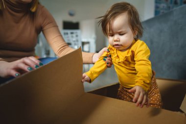 Evdeki karton kutuda annesinin yanında oynayan küçük beyaz bir kız çocuğu. Gerçek insanların ailesi ve büyüyen konsept fotokopi alanı.