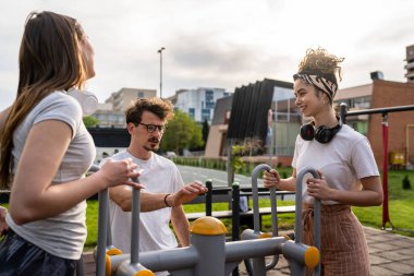 Bir grup arkadaş, erkek ve kadın, erkek ve genç, açık havada spor salonunda, modern binanın önünde antrenman yapıyorlar. Gerçek insanlar spor ve eğlence, sağlıklı yaşam tarzı kavramları geliştiriyorlar.
