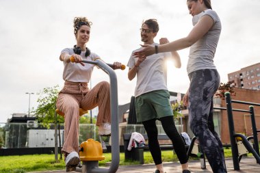 Bir grup arkadaş, erkek ve kadın, erkek ve genç, açık havada spor salonunda, modern binanın önünde antrenman yapıyorlar. Gerçek insanlar spor ve eğlence, sağlıklı yaşam tarzı kavramları geliştiriyorlar.