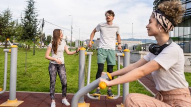 Bir grup arkadaş, erkek ve kadın, erkek ve genç, açık havada spor salonunda, modern binanın önünde antrenman yapıyorlar. Gerçek insanlar spor ve eğlence, sağlıklı yaşam tarzı kavramları geliştiriyorlar.