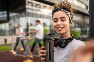 Beyaz kadın açık hava antrenmanı sırasında fren yapıyor açık hava spor salonunda barlarda dinleniyor el sıkışma aleti ile su içiyor ya da mutlu bir gülümsemeyle selfie fotokopi çekiyor.