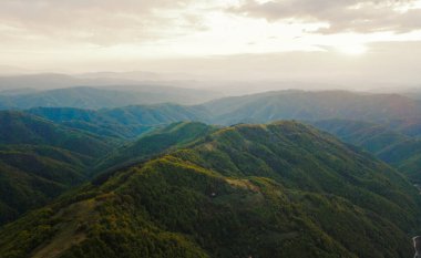 Günbatımının yüksek açılı hava görüntüsü güneş ışınları sonbahar veya kış günlerinde dağlık alanda ağaçlar ve ormanlar boyunca yolculuk ve tatil konsepti - Sırbistan 'daki Babin Zub Eski Dağı