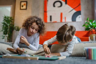 small boy and girl drawing on the green board at home two children brother and sister siblings or friends lying on the floor using chalk leisure and education real people family concept copy space