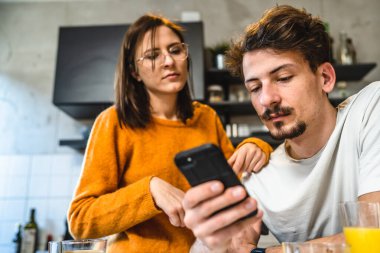 Two people young couple adult man and woman husband and wife or boyfriend with girlfriend in the kitchen in the morning with coffee juice mobile phone and digital tablet talking and chat daily routine