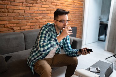 Yetişkin bir erkek, evdeki kanepede oturup uzaktan kumandayla uzaktan kumanda kullanan beyaz bir erkek.