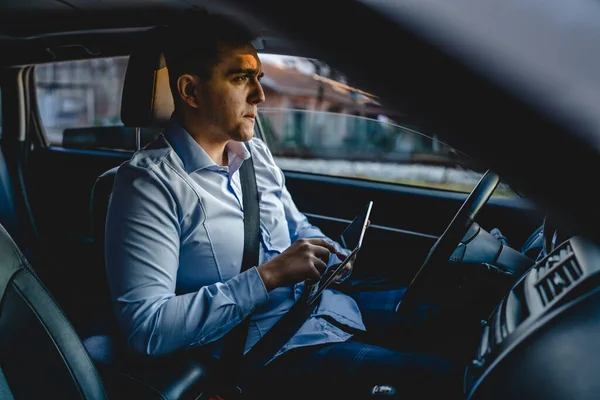 One man young adult manager or sales director business person sitting on the front seat of car using digital tablet to check road direction or order business details while waiting in the automobile