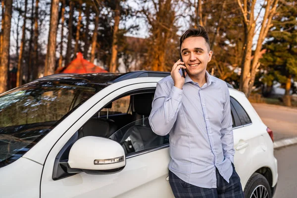 사업가가 자동차 실외에서 통화로 미소를 핸드폰을 사용하고 있습니다 — 스톡 사진