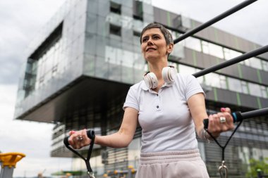 Bir kadın olgun ya da yaşlı, kauçuk elastik direnç bantlı beyaz kadın eğitimi. Açık spor salonunun spor salonundaki tüplerde. Sağlıklı yaşam tarzı konsepti.