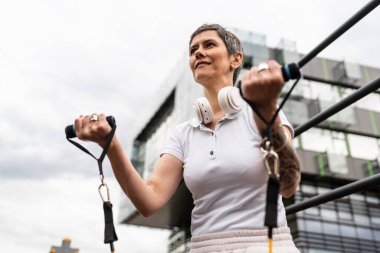 Bir kadın olgun ya da yaşlı, kauçuk elastik direnç bantlı beyaz kadın eğitimi. Açık spor salonunun spor salonundaki tüplerde. Sağlıklı yaşam tarzı konsepti.