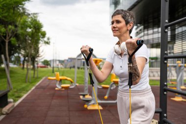 Bir kadın olgun ya da yaşlı, kauçuk elastik direnç bantlı beyaz kadın eğitimi. Açık spor salonunun spor salonundaki tüplerde. Sağlıklı yaşam tarzı konsepti.