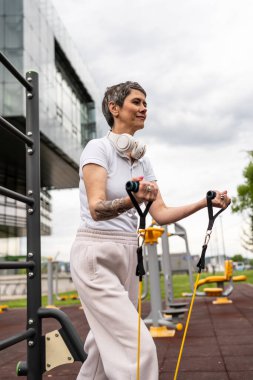 Bir kadın olgun ya da yaşlı, kauçuk elastik direnç bantlı beyaz kadın eğitimi. Açık spor salonunun spor salonundaki tüplerde. Sağlıklı yaşam tarzı konsepti.