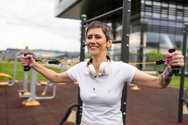 Bir kadın olgun ya da yaşlı, kauçuk elastik direnç bantlı beyaz kadın eğitimi. Açık spor salonunun spor salonundaki tüplerde. Sağlıklı yaşam tarzı konsepti.