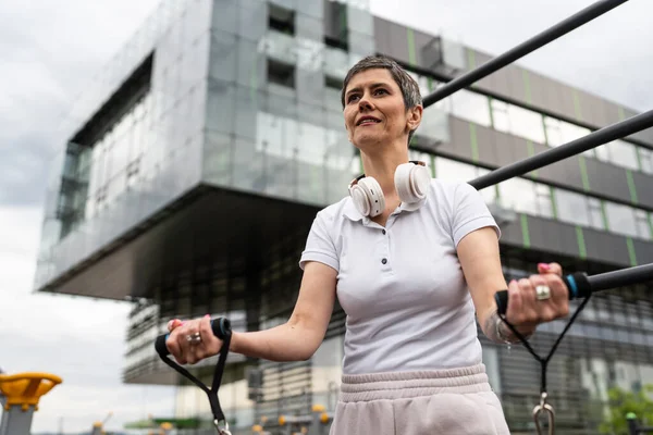 Bir kadın olgun ya da yaşlı, kauçuk elastik direnç bantlı beyaz kadın eğitimi. Açık spor salonunun spor salonundaki tüplerde. Sağlıklı yaşam tarzı konsepti.