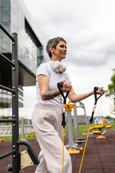 Bir kadın olgun ya da yaşlı, kauçuk elastik direnç bantlı beyaz kadın eğitimi. Açık spor salonunun spor salonundaki tüplerde. Sağlıklı yaşam tarzı konsepti.
