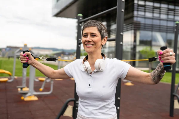 Bir kadın olgun ya da yaşlı, kauçuk elastik direnç bantlı beyaz kadın eğitimi. Açık spor salonunun spor salonundaki tüplerde. Sağlıklı yaşam tarzı konsepti.