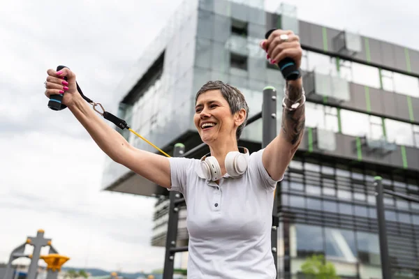 Bir kadın olgun ya da yaşlı, kauçuk elastik direnç bantlı beyaz kadın eğitimi. Açık spor salonunun spor salonundaki tüplerde. Sağlıklı yaşam tarzı konsepti.