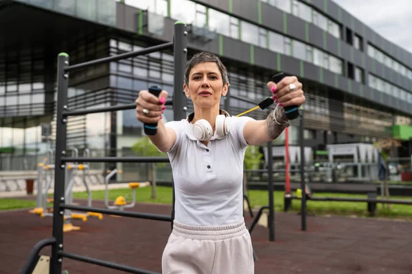 Bir kadın olgun ya da yaşlı, kauçuk elastik direnç bantlı beyaz kadın eğitimi. Açık spor salonunun spor salonundaki tüplerde. Sağlıklı yaşam tarzı konsepti.
