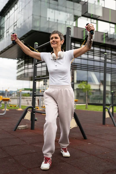 Bir kadın olgun ya da yaşlı, kauçuk elastik direnç bantlı beyaz kadın eğitimi. Açık spor salonunun spor salonundaki tüplerde. Sağlıklı yaşam tarzı konsepti.