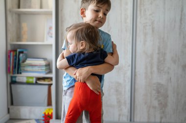 Erkek ve kız kardeş, küçük beyaz oğlan ve kız çocuk, daha yeni yürümeye başlamış çocuk ve anaokulu öğrencisi. Gündüz vakti aydınlık odada tek başına durup aile kavramını kopyalayarak büyümüş.