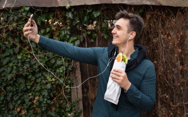 Sonbahar ya da kış günlerinde dışarıda dikilen bir adam, tişört giymiş sandviç turisti tutarken, dışarıda eski duvarın önünde beklerken cep telefonu kullanıyor. Gerçek insanlar uzay fast food konseptini kopyalıyor.