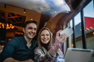 Kafkasyalı iki genç çift, kadın ve erkek arkadaş veya erkek arkadaş veya kız arkadaş selfie çekiyorlar ya da kafeteryada oturup eğlenirken ve romantizm yaparken görüntülü görüşme yapıyorlar.