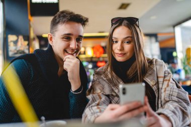Kafkasyalı iki genç çift, kadın ve erkek arkadaş veya erkek arkadaş veya kız arkadaş selfie çekiyorlar ya da kafeteryada oturup eğlenirken ve romantizm yaparken görüntülü görüşme yapıyorlar.