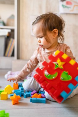 Küçük, beyaz bir kız. Evdeki fotokopi odasında yerde oynuyor. Elinde plastik oyuncaklar var.