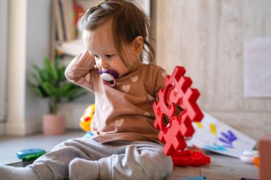 Küçük beyaz bir kız çocuğu elinde cep telefonuyla ev fotokopi odasının zemininde oynuyor.